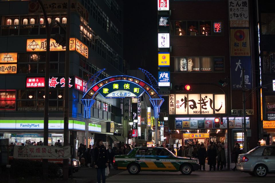 Shinjuku street at night featuring an illuminated archway, glowing signs, and a green taxi.