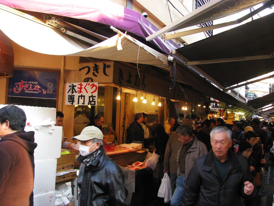 People browse fresh seafood counter displays at an outdoor market in Tsukiji.