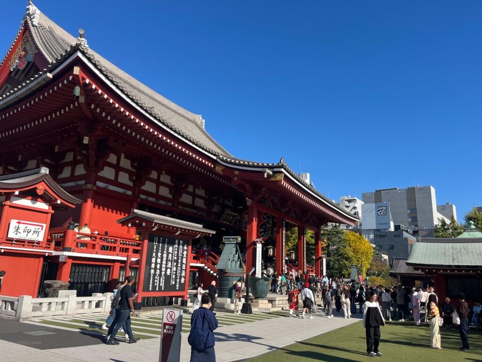 Red and white main hall of Senso-ji Temple with visitors gathered under a clear blue sky.